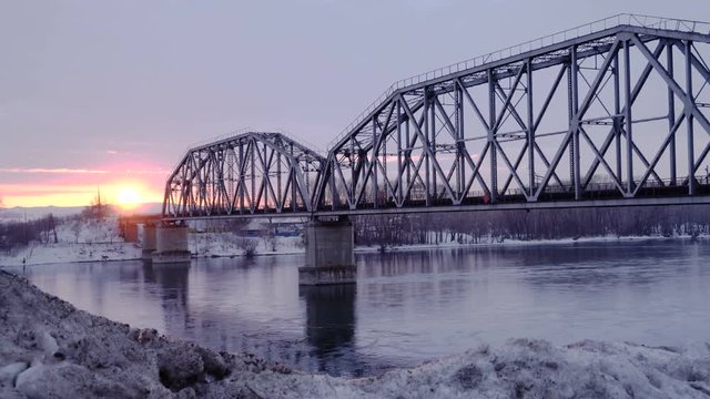 Time lapse of railway bridge over the river at dawn with a mountain forest and traffic highway in the background.