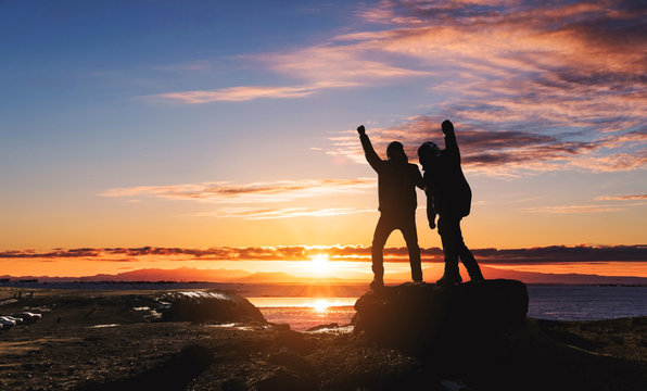 Silhouette two man success achievement goals, rise hand up on peak mountain, in morning sunrise