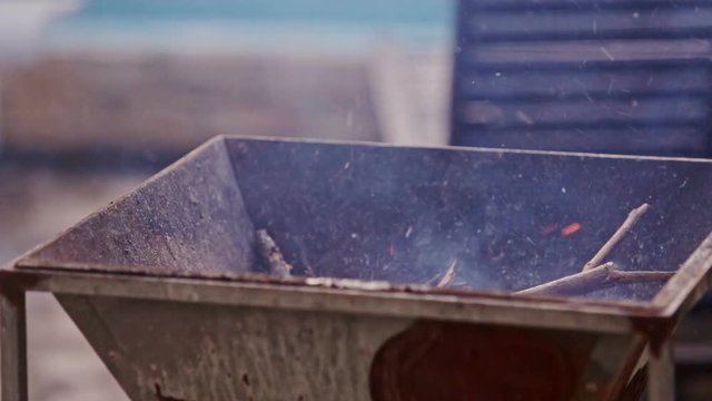 Closeup Person Waves Board to Burn Dry Sticks in Metal Grill