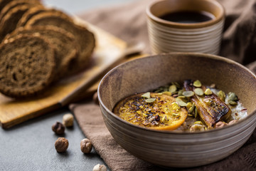 porridge with fried banana and orange. Bowl of oatmeal porridge with banana, Cinnamon. Hot and healthy food for Breakfast, with toast and coffee, on a wood round table with a butter knife.