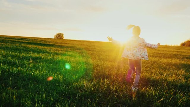 A carefree child runs happily through the green meadow. The girl enjoys a beautiful day and a beautiful sunset