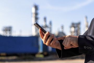 Businessman checking around oil refinery plant and container on smart phone