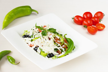 Traditional classic Shopska salad with tomatoes, peppers, cucumbers and cheese in white dish on white wooden table. Bulgarian cuisine, Balkan culture