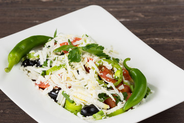 Traditional classic Shopska salad with tomatoes, peppers, cucumbers and cheese in white dish on grey wooden table. Bulgarian cuisine, Balkan culture
