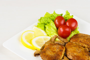 Pork fillet steak with cherry tomatoes, lemon and a lettuce in white dish on white background