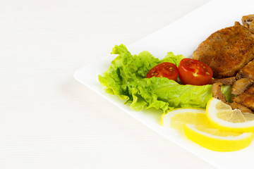 Pork fillet steak with cherry tomatoes, lemon and a lettuce in white dish on white background