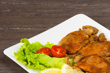 Pork fillet steak with cherry tomatoes, lemon and a lettuce in white dish on grey background.