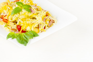 Tagliatelle pasta with pesto sauce, bacon, Gauda, Cheddar, Emmental cheese and basil leaves in white plate on white wooden background. Close up image - healthy homemade pasta