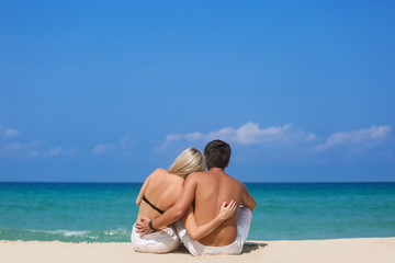 Romantic couple sitting on the beach and enjoying beautiful sea view, side view, spending time together, summer vacation concept