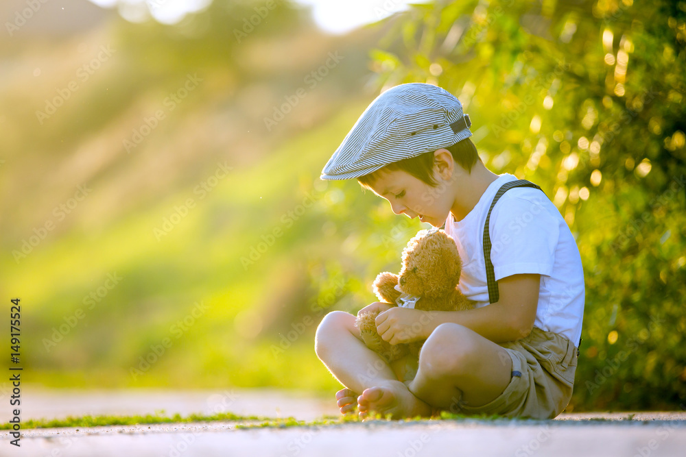 Poster Sweet boy, playing with teddy bear on a small rural path on sunset