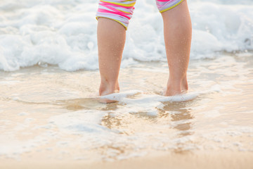 Children's legs stand on the beach.