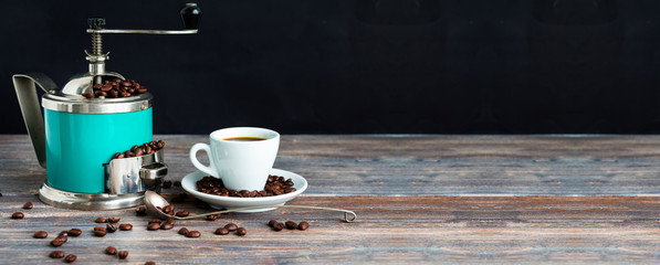 Coffee mill and cup of espresso. Concept of coffee drinking tradition. Selective focus. Wooden table, coffee beans. Black background. Wide panoramic image. Copy space.