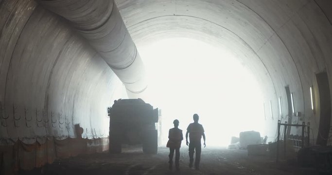 silhouette of construction workers walking on a large tunnel construction site