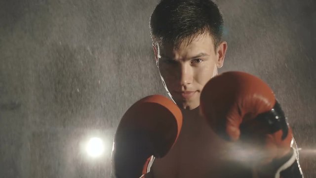 Portrait of boxer stands under water splashing on ring looking at camera. Slowly