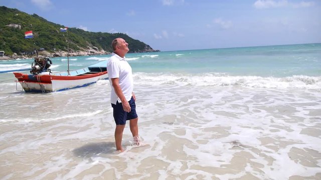 Happy Senior Man Walking On Tropical Beach in Waves