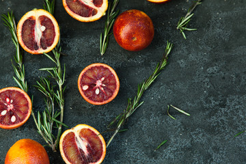 Red Sicilian orange whole and cut on a dark background with branches of rosemary. Daylight, open space for your text.