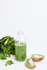 Green cocktail in a bottle and in a glass with spinach, mint, rosemary, kiwi and apple on a light background.