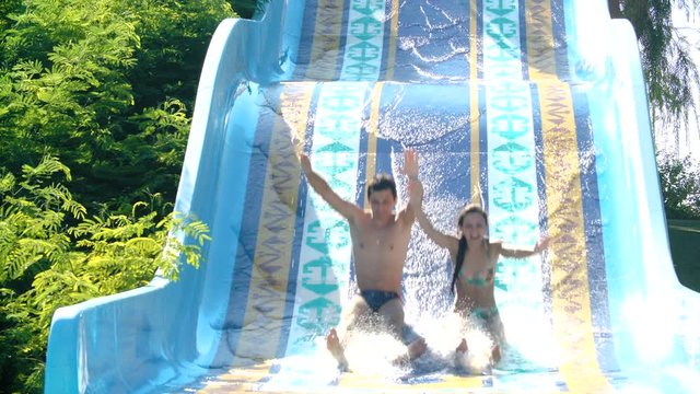 Happy couple sliding down water slide smiling in sunny summer. water Park.