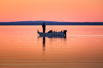 One man fishing from small boat at sunset