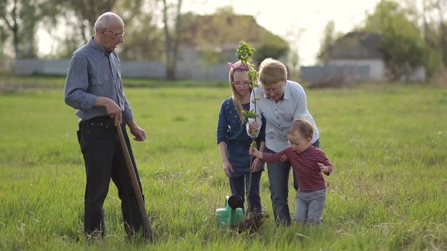 Multi generation family planting tree outdoor.