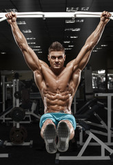 Fototapeta na wymiar Muscular man working out in gym, doing stomach exercises on a horizontal bar, strong male naked torso abs