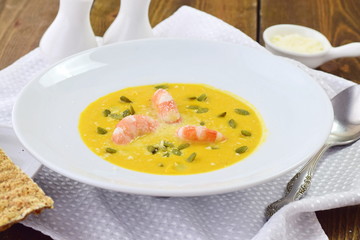 Pumpkin puree soup with prawns in a white plate on a wooden background. Healthy eating concept