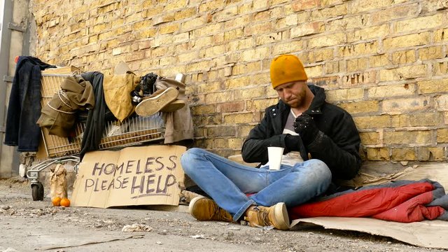  Homeless man counting how much money he got, holding paper cup in the hands.