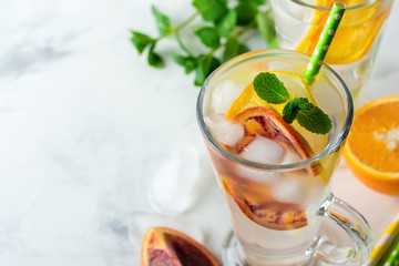 Cold and refreshing infused detox water with  orange, lemon and ice  in glass on a light background. Selective focuse.