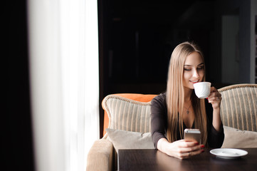 Young woman drinking coffee in a cafe and using a mobile phone