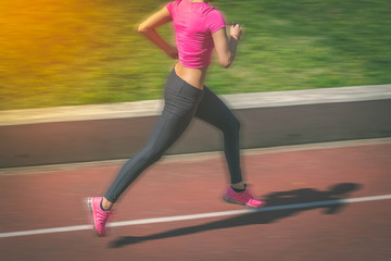 Female jogger running on athletic track. Motion blur.