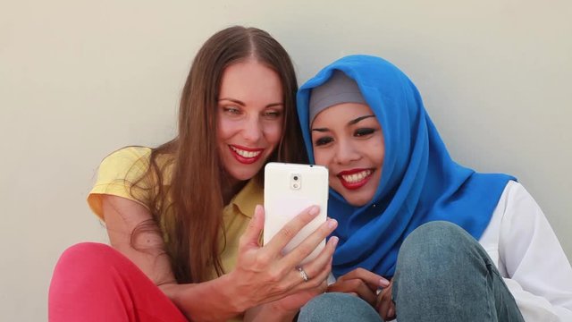 caucasian woman using phone together with asian muslim girl