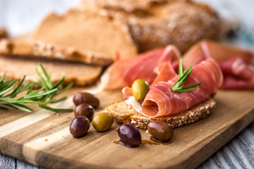 Prosciutto with olives on wooden background