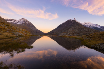 Fototapeta na wymiar High altitude alpine lake in idyllic land with reflection of majestic rocky mountain peaks glowing at sunset. Wide angle view on the Alps.