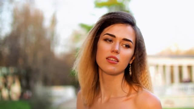 Attractive girl with black brows and curly hair looks at camera and talks during photoshoot.