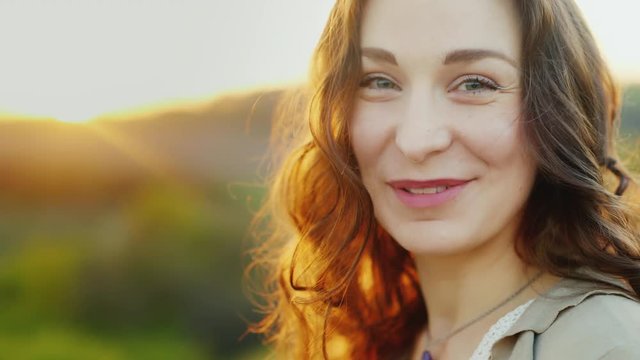 Portrait of an attractive middle-aged woman. He looks and smiles at the camera. Behind the setting sun beautifully highlights her hair