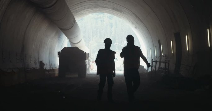silhouette of construction workers walking on a large tunnel construction site