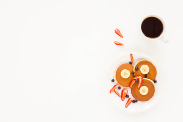 Summer breakfast of pancakes with fresh fruit, banana, blueberries, strawberry, cup of black coffee on white background. Mock up, top view, flat lay