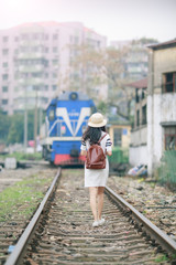 Naklejka premium Beautiful girl with backpack walking on railway tracks at railway station