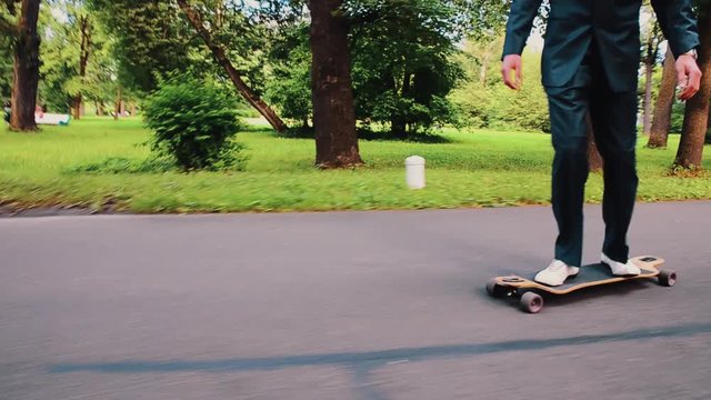 Man with mustache in dinner jacker, sunglasses, hat ride on skateboard on road. Summer day