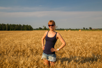 A young beautiful woman standing at wheat field under sunlight.	