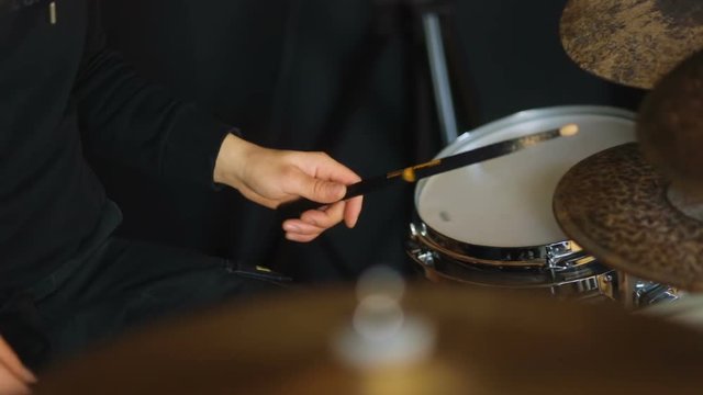 Man in shadeless black style playing on the drums side-view