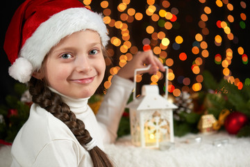 child girl portrait with christmas decoration, dark background with lights, face expression and happy emotions, dressed in santa hat, winter holiday concept