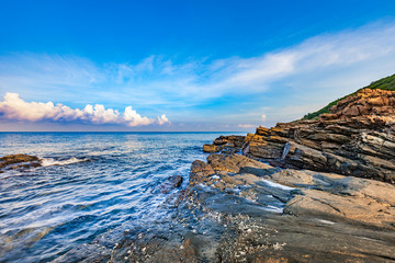 Rocky seashore in morning sunrise with bright blue sky and clouds