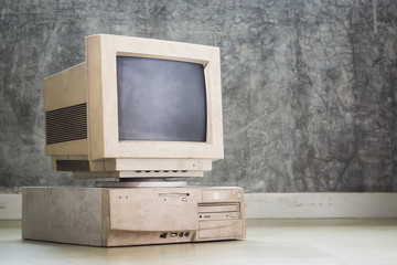 old and obsolete computer set on the floor with grunge concrete wall background, vintage color tone