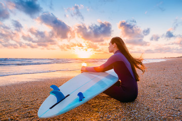 Beautiful surfer girl with surfboard on the beach at sunset