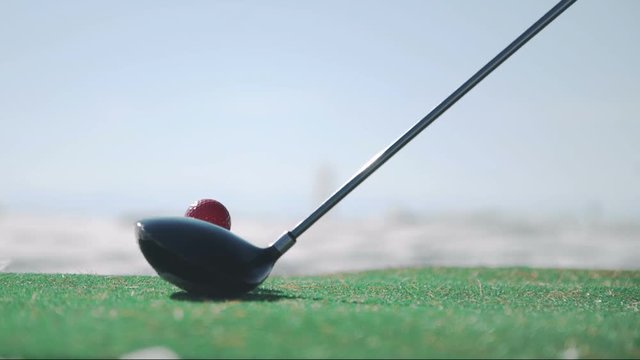 man playing golf using synthetic grass carpet in winter outdoors. red ball set on plastic tee, stick slightly knocked far away. Golfers hit sweeping on snowy icy surface. Close-up shooting of bandy
