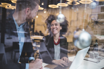 Multi racial business man and woman working together in modern cafe or restaurant. View from street through window glass. - Powered by Adobe