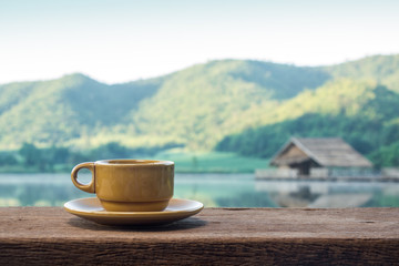 coffee cup on old wood table against view of morning sunlight, reservoir, hut and mountain