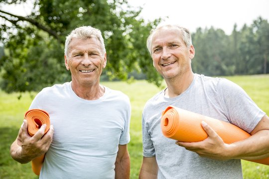 Two men with yoga mats, smiling