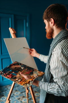 Artist with palette and brush in front of easel